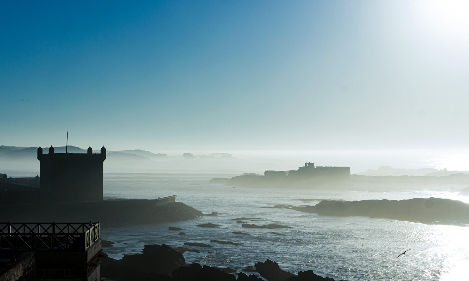 silhouette of lighthouse on top of hill by the sea during daytime